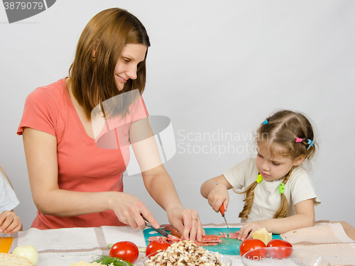 Image of Mom teaches daughter to a six-year cut with a knife products for cooking at the kitchen table