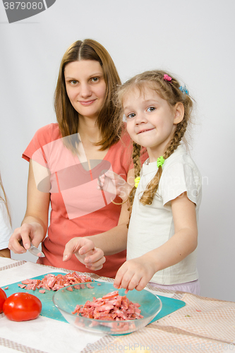 Image of Little six year old girl helps mother to cook at the kitchen table