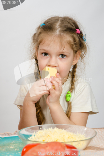 Image of Five-year girl with pigtails eating cheese at the table in front of her is a plate of grated cheese