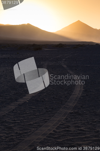 Image of Wheel tracks in sand and dramatic landscape.