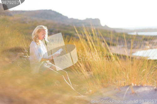 Image of Woman enjoys reading on beautiful sandy beach.