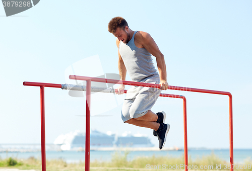 Image of young man exercising on parallel bars outdoors