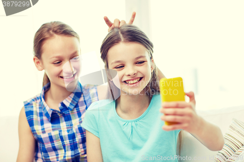 Image of happy girls with smartphone taking selfie at home