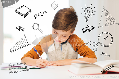 Image of smiling student boy writing to notebook at home