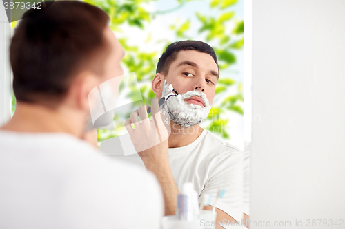 Image of man shaving beard with razor blade at bathroom