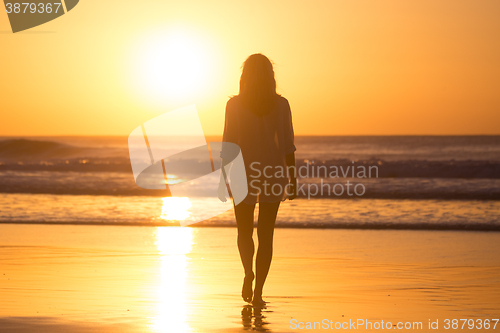 Image of Lady walking on sandy beach in sunset.