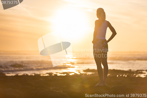 Image of Woman on sandy beach watching sunset.