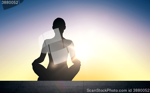 Image of woman meditating in yoga lotus pose over sun light