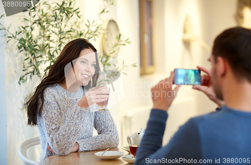 Image of man taking picture of woman by smartphone at cafe