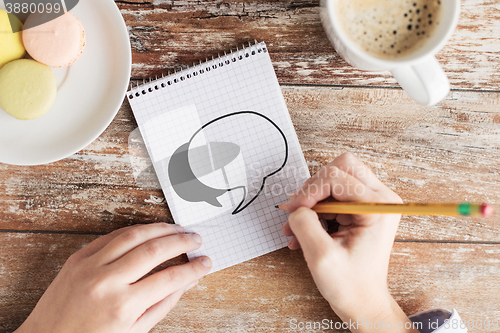 Image of close up of hands drawing text bubble in notebook