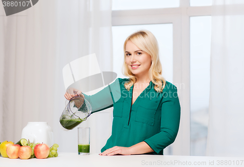 Image of happy woman with blender jug pouring juice at home