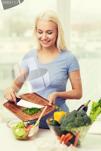 Image of smiling woman cooking vegetable salad at home