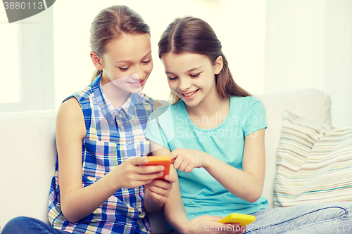 Image of happy girls with smartphones sitting on sofa