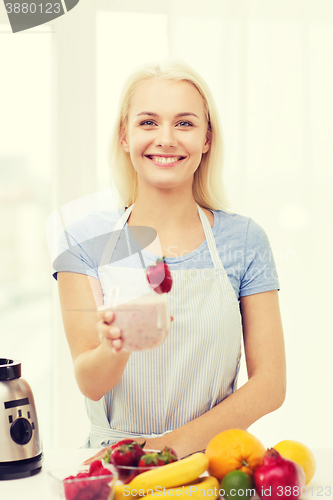 Image of smiling woman holding glass of fruit shake at home