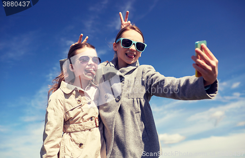 Image of happy girls with smartphone taking selfie outdoors