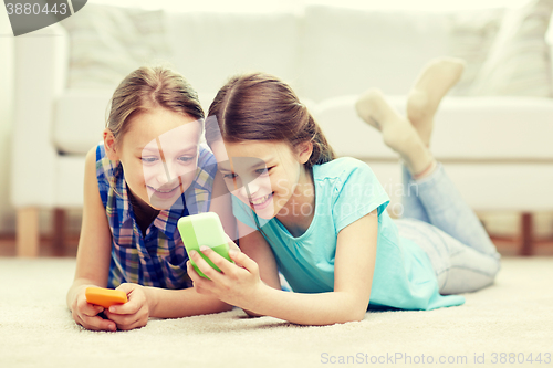 Image of happy girls with smartphones lying on floor