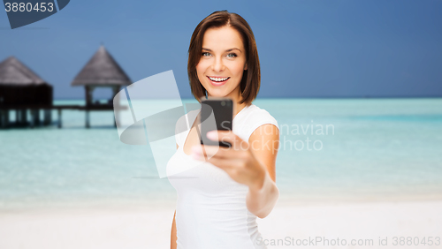 Image of happy woman taking picture by smartphone on beach