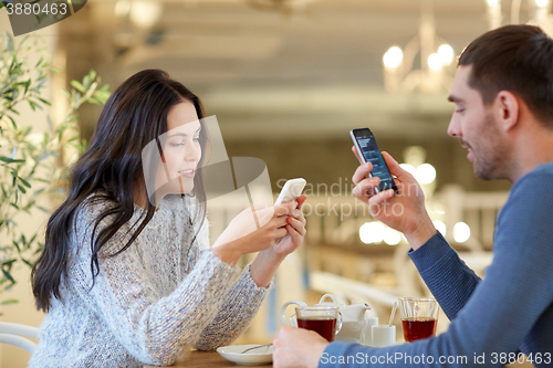 Image of happy couple with smartphones drinking tea at cafe