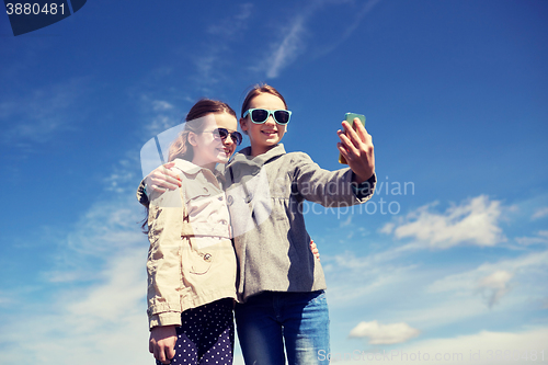 Image of happy girls with smartphone taking selfie outdoors