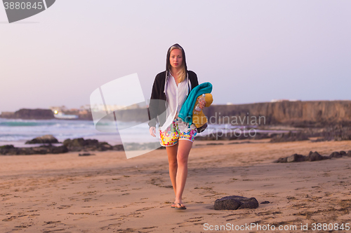 Image of Sporty woman walking on sandy beach in sunset.