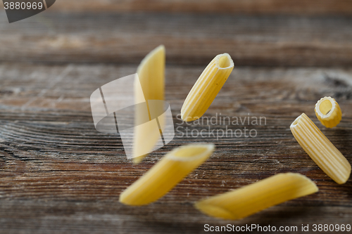 Image of Falling penne pasta. Flying yellow raw macaroni over black background.