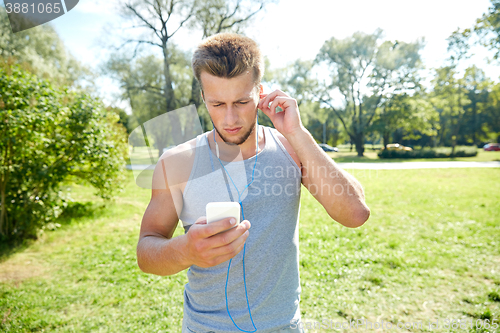 Image of young man with earphones and smartphone at park