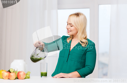 Image of happy woman with blender jug pouring juice at home