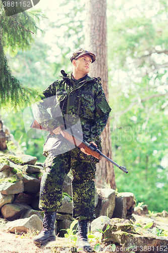 Image of young soldier or hunter with gun in forest