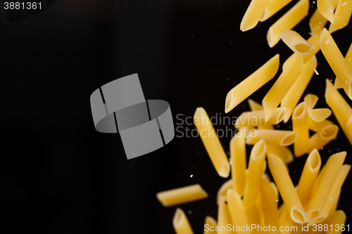 Image of Falling penne pasta. Flying yellow raw macaroni over black background.