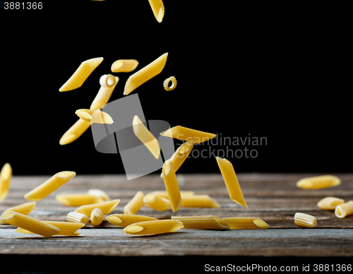 Image of Falling penne pasta. Flying yellow raw macaroni over black background.