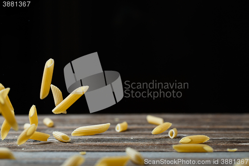 Image of Falling penne pasta. Flying yellow raw macaroni over black background.