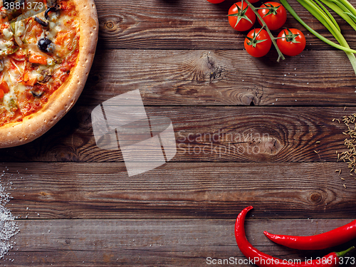 Image of Italian pizza with tomatoes on a wooden table, top view.