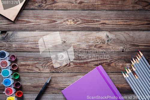 Image of Watercolors, color pencils and sketchbook on wooden table. Flat lay photo with empty space for logo, text.