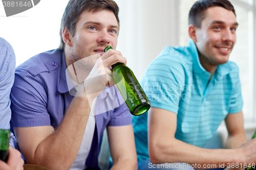 Image of happy male friends drinking beer at home