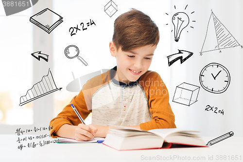 Image of smiling student boy writing to notebook at home