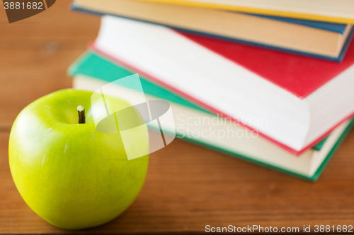 Image of close up of books and green apple on wooden table