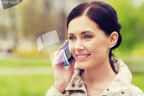 Image of smiling woman calling on smartphone in park