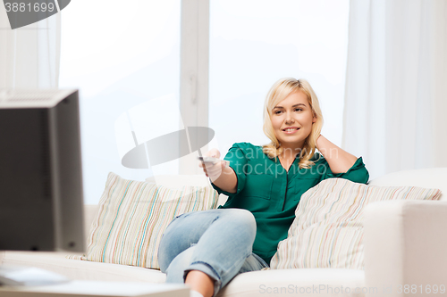 Image of smiling woman with remote watching tv at home