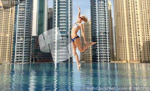 Image of happy young woman jumping over dubai city pool