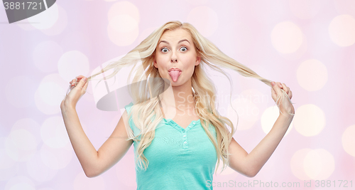 Image of happy young woman showing tongue and holding hair