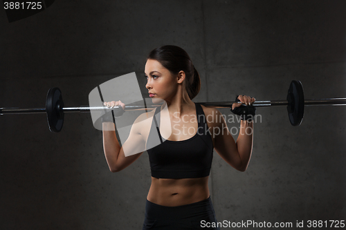 Image of young woman flexing muscles with barbell in gym