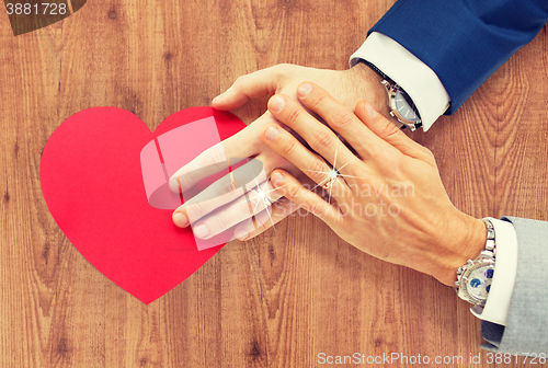 Image of close up of male gay couple hands with red heart