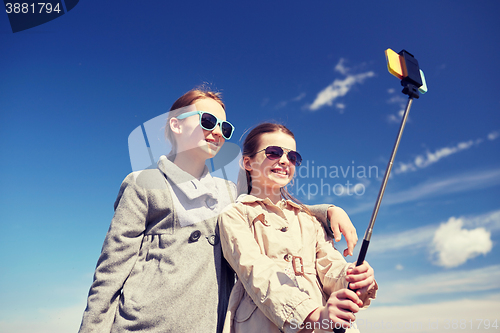 Image of happy girls with smartphone selfie stick