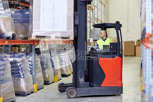 Image of man with tablet pc operating forklift at warehouse