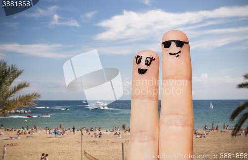 Image of close up of two fingers with smiley faces on beach