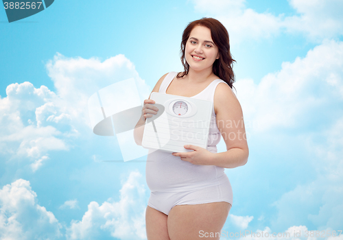 Image of happy young plus size woman holding scales