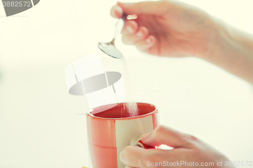 Image of close up of woman hands adding sugar to tea cup