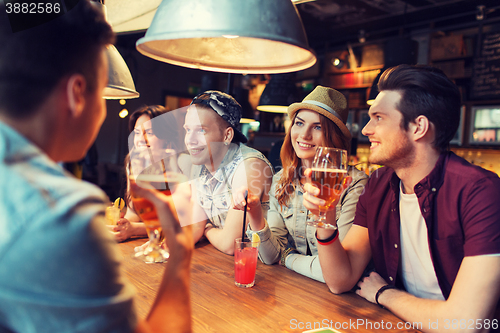 Image of happy friends with drinks talking at bar or pub