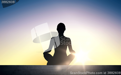 Image of woman meditating in yoga lotus pose over sun light