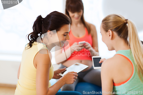 Image of happy pregnant women with gadgets in gym